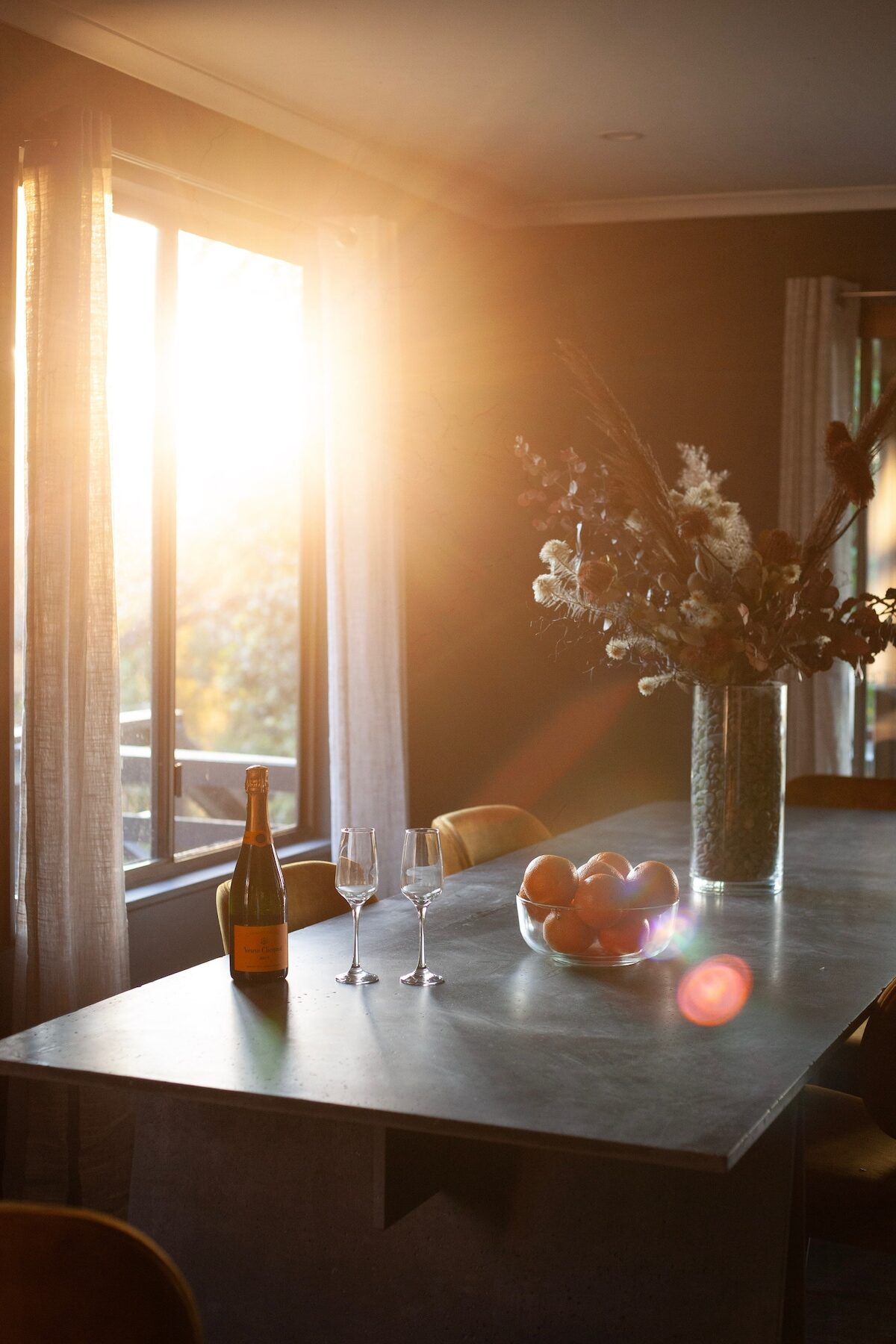 Dining table at golden hour set with champagne, glasses, oranges and dried flowers